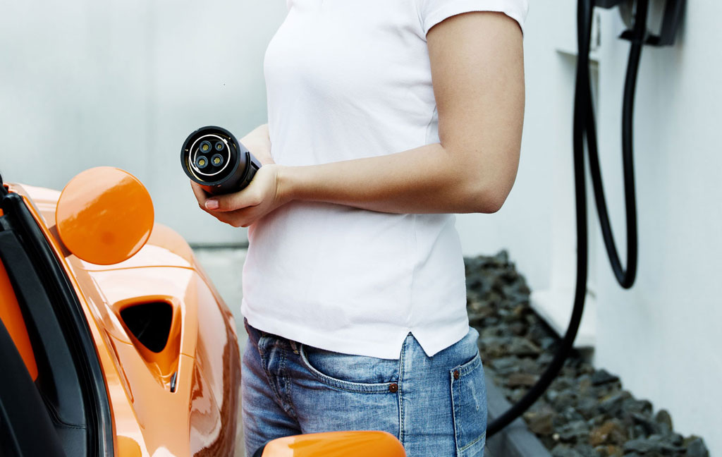 Frau mit Ladestecker am Auto